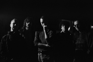 Bandfoto Bash Tru: Fünfköpfige Band im Dunkeln (Schwarzweiß)

Fünf Personen stehen dicht nebeneinander in einem dunklen Raum. Das Bild ist in Schwarzweiß gehalten und nur seitlich beleuchtet, wodurch Gesichter und Oberkörper teilweise im Schatten liegen. Die Stimmung wirkt reduziert und ruhig.