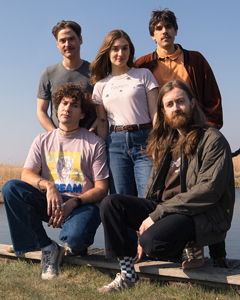 Bandfoto How to make friends: Fünfköpfige Band im Freien
Fünf Musiker posieren auf einer Wiese unter freiem Himmel. Zwei Bandmitglieder sitzen im Vordergrund, die anderen stehen dahinter. Die Gruppe trägt legere Kleidung und ist vor einem klaren blauen Himmel fotografiert.