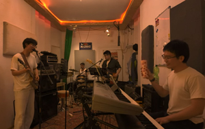 Bandfoto Groovy Habit: Band im Proberaum
Vier Musiker spielen gemeinsam in einem kleinen, warm beleuchteten Proberaum. Im Vordergrund sitzt ein Musiker am Keyboard, links steht ein Musiker am Mikrofon. Im Hintergrund sind Schlagzeug, Gitarre, Verstärker, Mikrofone und weitere Musikausrüstung zu sehen.