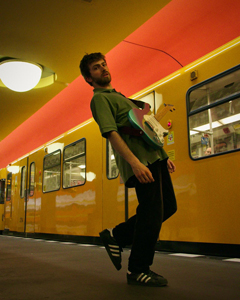 Bandfoto Lorenzo: Ein Mann mit E-Gitarre steht auf einem Bahnsteig vor einer gelben U-Bahn. Das Licht ist warm, die Decke leuchtet gelb und orange. Er wirkt lässig und leicht in Bewegung.